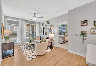 Spacious living room with a ceiling fan and a French door with large picture windows next to a couch and armchair with coffee table on area rug and wood floors at MAA Vale luxury apartments in Raleigh, NC