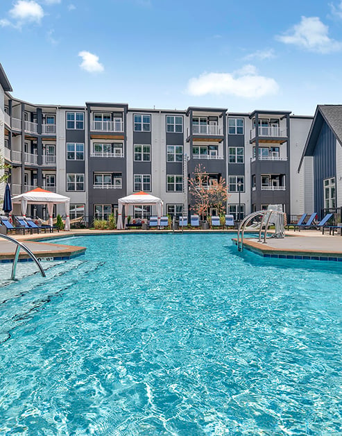 Sparkling pool with entrance steps with lounge chairs and two white cabanas situated next to the apartment complex at MAA Vale luxury apartments in Raleigh, NC