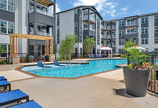 Long view of resort-style swimming pool with a sundeck and entrance steps next to lounge chairs situated near the apartment complex at MAA Vale luxury apartments in Raleigh, NC