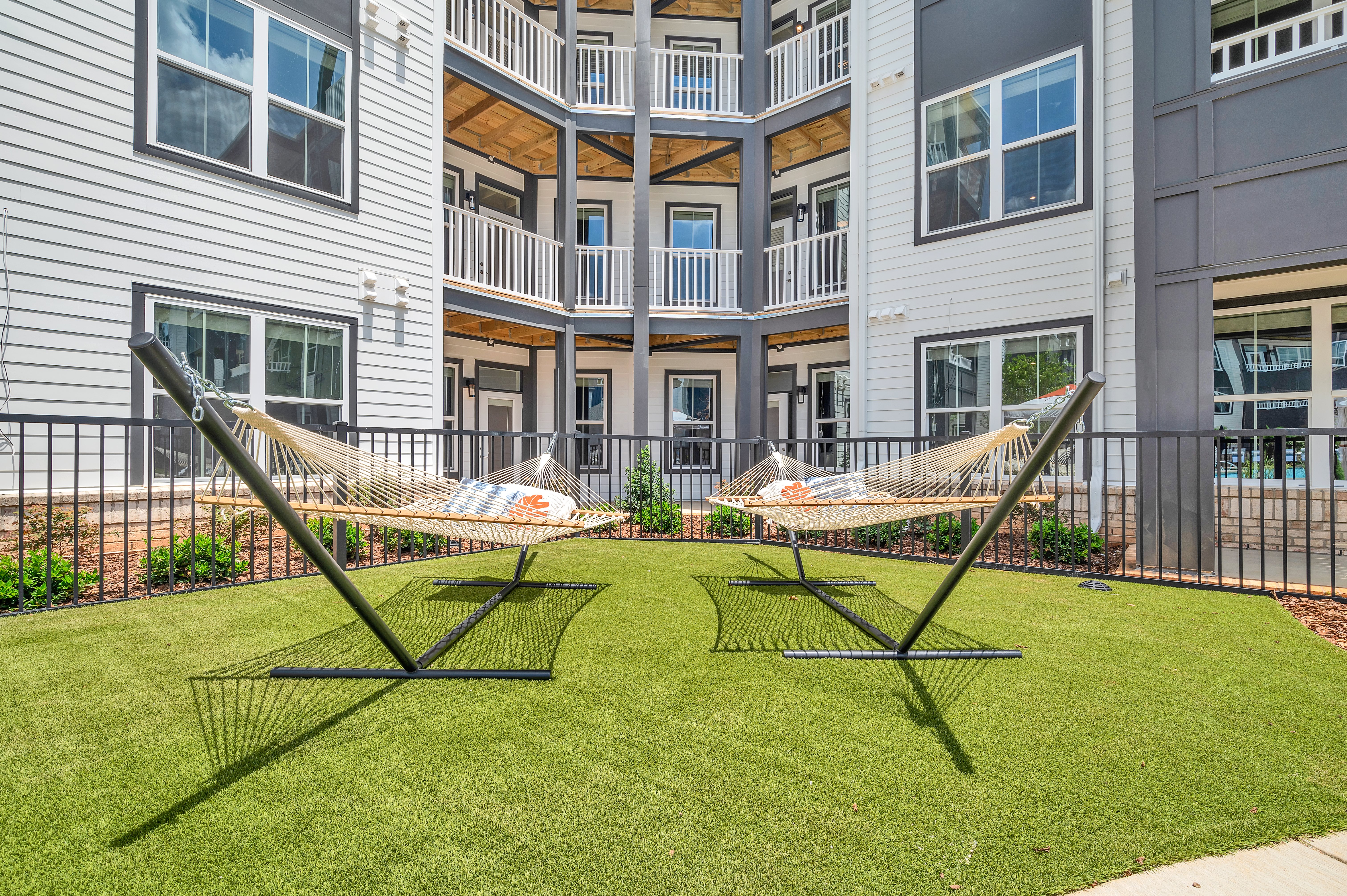 Poolside gated grassy courtyard area with two hammocks situated next to apartment complex at MAA Vale luxury apartments in Raleigh, NC