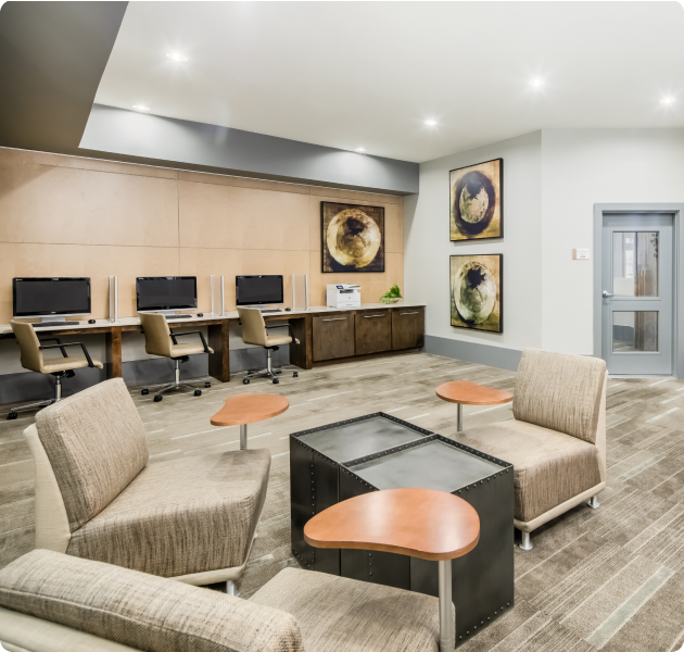 Community business center with computer workstations with and sitting lounge area with armchairs next to entrance at MAA Acklen luxury apartments in Nashville, TN