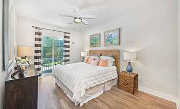 Model bedroom with sliding glass doors and a ceiling fan with wall art over the bed and nightstands on wood floors at MAA Acklen luxury apartments in Nashville, TN