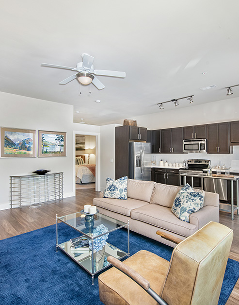 Living room with ceiling fan and sitting area with glass top coffee table on an area rug with wood floors next to the kitchen at MAA Acklen luxury apartments in Nashville, TN