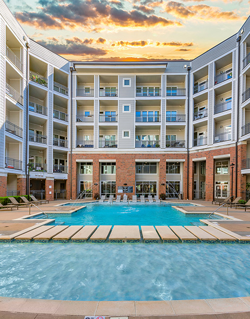 Long view of resort-style swimming pool with sundeck, entrance steps with handrails, pool fountain and lounge chairs situated next to the apartment complex at MAA Acklen luxury apartments in Nashville, TN