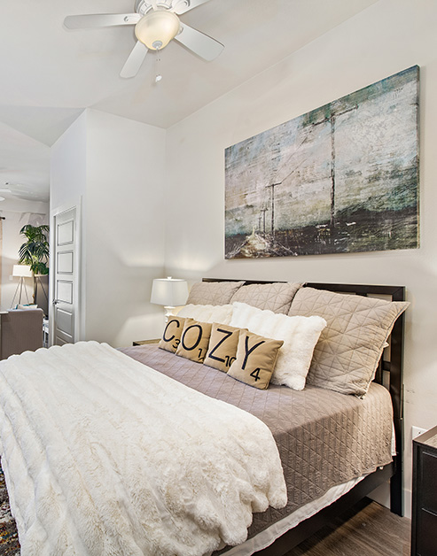 Studio bedroom space with a ceiling fan and wall art with lamps on night stands and wood floors at MAA Acklen luxury apartments in Nashville, TN