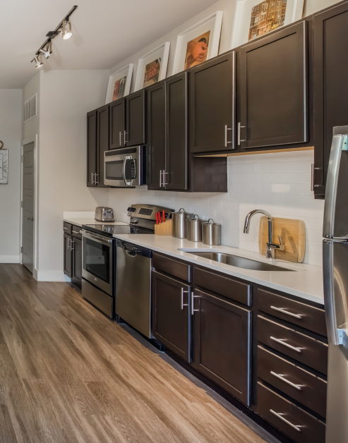 Modern kitchen with ceiling track lighting, dark brown cabinets with stainless-steel appliances and white countertops with white backsplash and wood floors at MAA Acklen luxury apartments in Nashville, TN