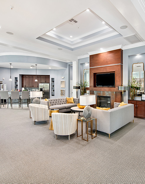 Modern clubhouse with ornate beveled ceilings, wall-mounted TV and fireplace with multiple sitting areas next to an open kitchen bar at MAA Bellevue luxury apartments in Nashville, TN