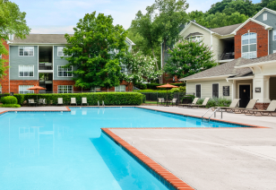 Side view of resort-style swimming pool with lounge chairs surrounded by lush trees next to the clubhouse at MAA Bellevue luxury apartments in Nashville, TN