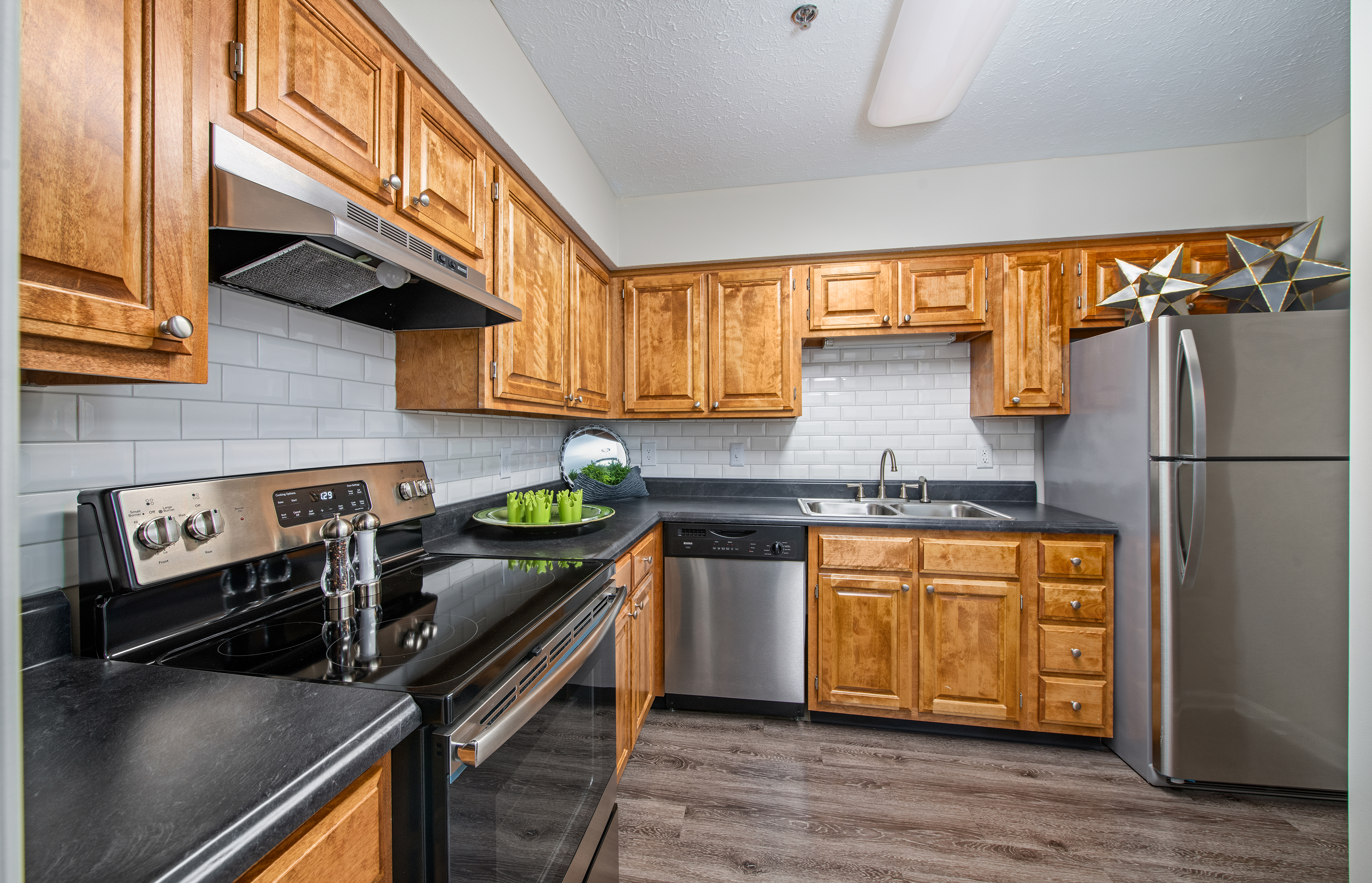 Apartment kitchen with black countertops, stainless-steel appliances with wood cabinets with white tile backsplash and wood floors at MAA Brentwood luxury apartments in Nashville, TN
