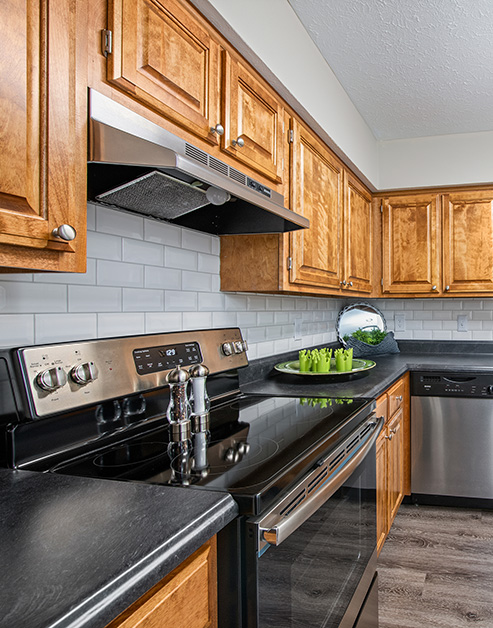 Stylish kitchen with light wood cabinets and white tile backsplash, black countertops with stainless-steel appliances and wood floors at MAA Brentwood luxury apartments in Nashville, TN