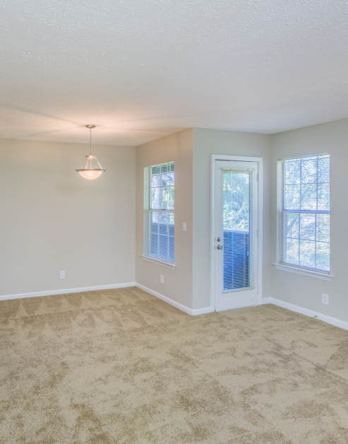 Empty carpeted living room with a hanging light fixture, French door and windows in natural light at MAA Brentwood luxury apartments in Nashville, TN