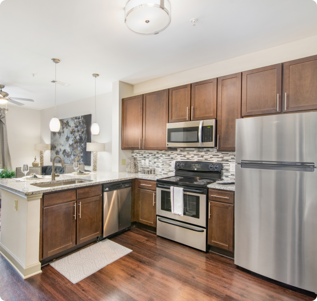 Apartment open-space kitchen with stainless-steel appliances, granite countertops, and wood cabinets on wood floors at MAA Charlotte Ave luxury apartments in Nashville, TN