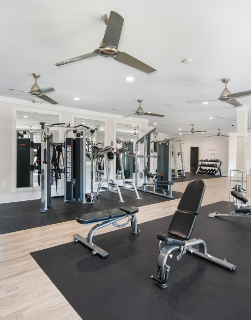 Fitness center with ceiling fans, adjustable workout bench and other gym equipment next to large wall mirrors at MAA Charlotte Ave luxury apartments in Nashville, TN