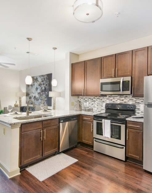 Open-style kitchen with wood cabinets and stainless-steel appliances, tiled backsplash and granite countertops and wood floors at MAA Charlotte Ave luxury apartments in Nashville, TN