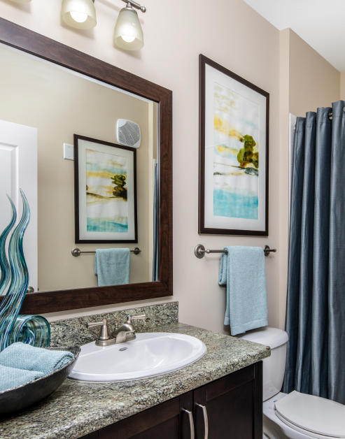 Modern bathroom with sleek light fixtures above a framed vanity mirror and sink with dark brown cabinets and blue shower curtains at MAA Cool Spring luxury apartments in Franklin, TN
