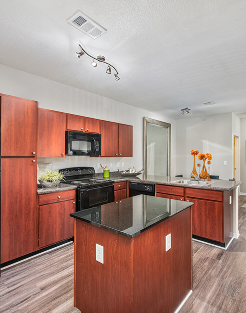 Stylish kitchen with ceiling track lights and dark countertops with cherry wood cabinets, upgraded appliances and kitchen island on wood floors at MAA Indian Lake luxury apartments in Hendersonville, TN