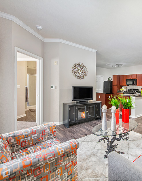 A model living room with a TV on a gray cabinet, couch sitting area with oval glass top coffee table on an area rug with wood floors at MAA Indian Lake luxury apartments in Hendersonville, TN