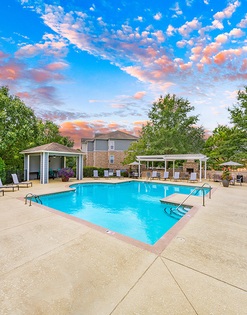 Side view of pool with multiple pergolas and lounge chairs surrounded by lush greenery at MAA Indian Lake luxury apartments in Hendersonville, TN