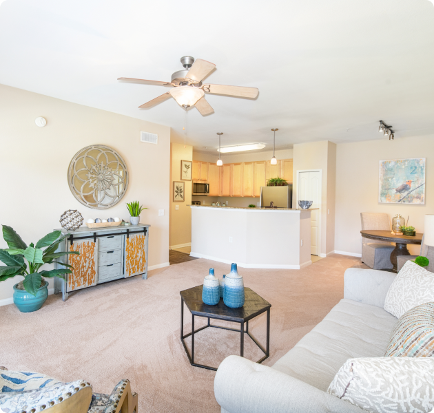 Model apartment living room with large carpeted space with a white couch and a coffee table next to open dining area and kitchen at MAA Kennesaw Farms luxury apartments in Gallatin, TN