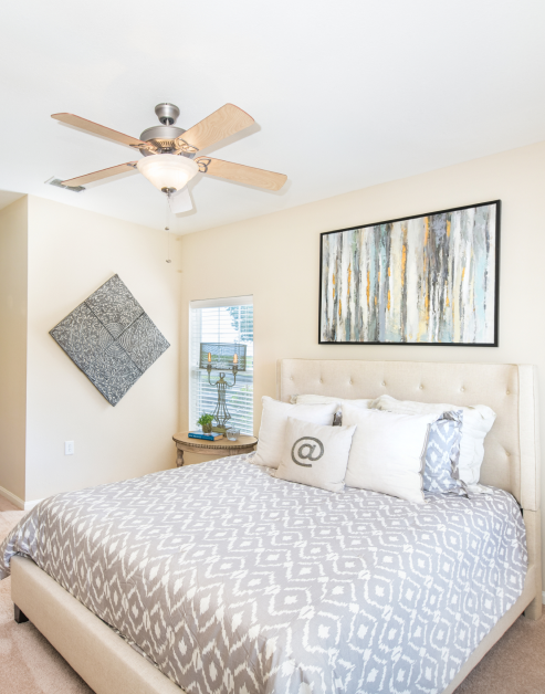 Bedroom with ceiling fan, wall painting over the bed and bedside table with lamp next to a window with blinds at MAA Kennesaw Farms luxury apartments in Gallatin, TN