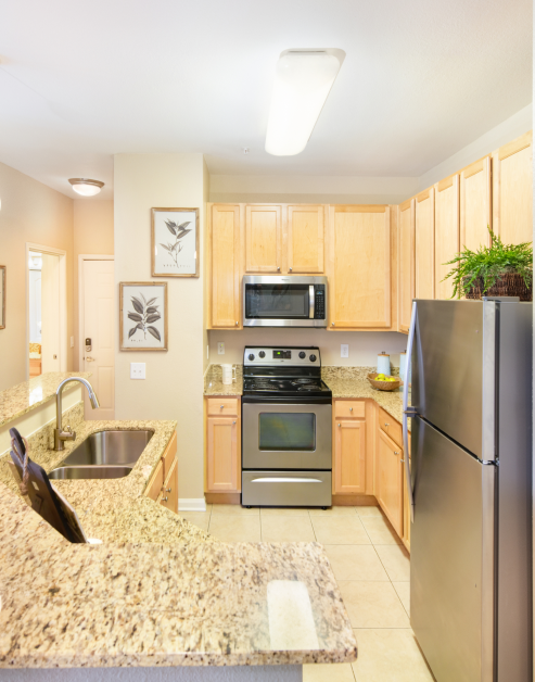 Modern-style kitchen with light brown cabinets, stainless steel appliances, granite countertops with double sink and tile floors at MAA Kennesaw Farms luxury apartments in Gallatin, TN