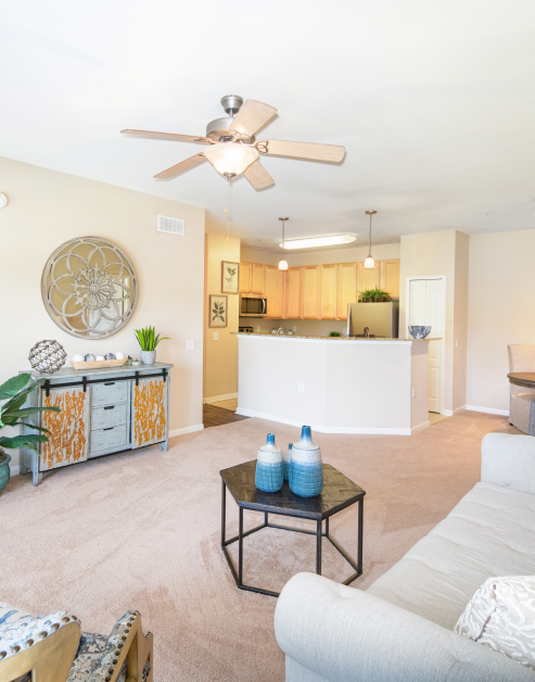 Carpeted living room with ceiling fan, decorative round wall mirror above the cabinet and a white couch with a octagon coffee table at MAA Kennesaw Farms luxury apartments in Gallatin, TN