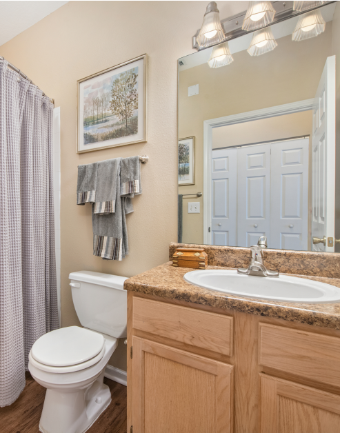 Bathroom with sleek light fixtures above vanity mirror and sink with wood cabinets on wood floors at MAA Monthaven Park luxury apartments in Hendersonville, TN