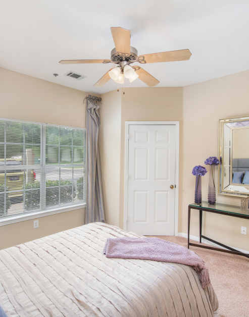 Bedroom with light-colored walls, ceiling fan and a window with blinds and curtains next to a closet door at MAA Monthaven Park luxury apartments in Hendersonville, TN