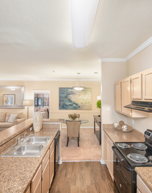 Open-style kitchen with light wood cabinets, upgraded appliances and bar top counter next to dining area with a glass table at MAA Monthaven Park luxury apartments in Hendersonville, TN