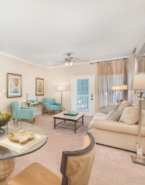 A spacious living room with a ceiling fan, cream-colored couch and armed chairs with a coffee table next to a French door at MAA Monthaven Park luxury apartments in Hendersonville, TN