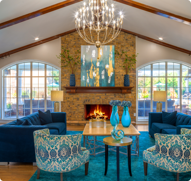 Community clubhouse with vaulted ceiling and a grand chandelier, sitting area with blue-toned furniture and coffee table with a blue area rug on wood floors at MAA Murfreesboro luxury apartments in Murfreesboro, TN