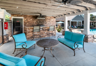 Poolside covered patio with ceiling fans, outdoor grilling station and multiple sitting areas with blue cushions at MAA Murfreesboro luxury apartments in Murfreesboro, TN