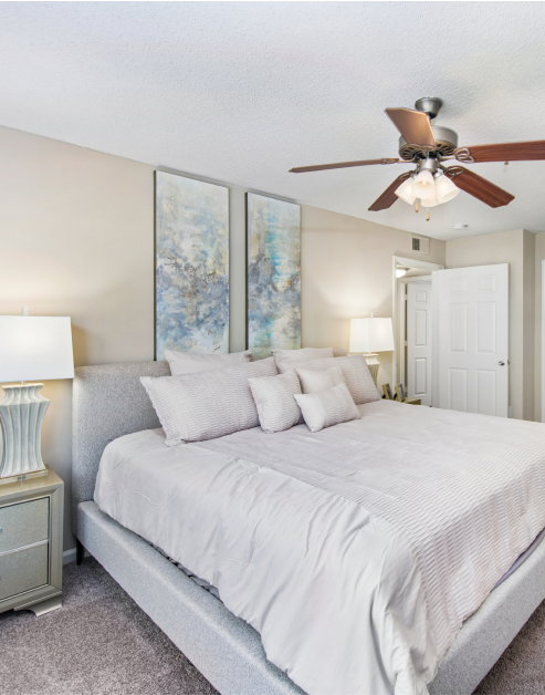 Carpeted bedroom with ceiling fan, night stands with lamps and white bedding with accent pillows at MAA Nashville West luxury apartments in Nashville, TN