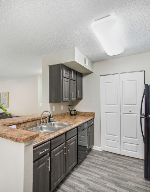 Open-style kitchen with double sink and bar top counter with dark grey cabinets on wood floors at MAA Nashville West luxury apartments in Nashville, TN