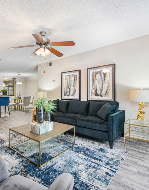 Living room with ceiling fan and a black couch with coffee table on an area rug and wood floors at MAA Nashville West luxury apartments in Nashville, TN