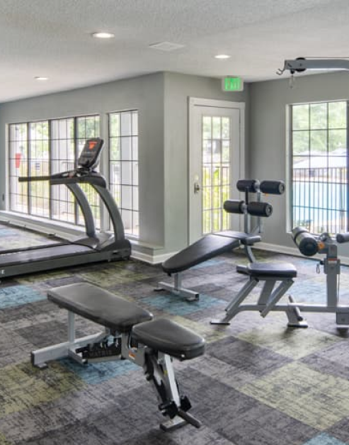 Spacious carpeted fitness center with treadmills and other workout machines next to large picture windows and a French door at MAA Park luxury apartments in Hermitage, TN