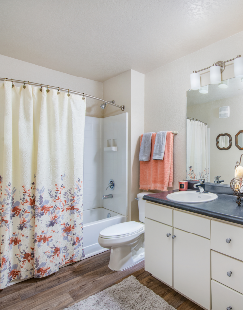 Bathroom with sleek light fixtures above vanity mirror and sink on black granite countertop with white cabinets and wood floors at MAA Sam Ridley luxury apartments in Smyrna, TN