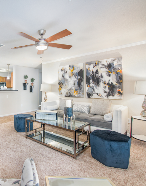 Model living room with ceiling fan, abstract wall art above white couch with accent pillows with a glass top coffee table at MAA Sam Ridley luxury apartments in Smyrna, TN