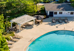 Aerial view of pool area with lounge chairs, pergola, sun umbrella with table and chairs surrounded by lush greenery at MAA Sam Ridley luxury apartments in Smyrna, TN