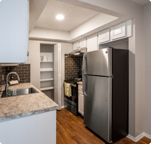 Apartment kitchen with white cabinets and a built-in pantry, granite countertops and stainless steel appliances on wood floors at MAA Barton Skyway luxury apartments in Austin, TX.