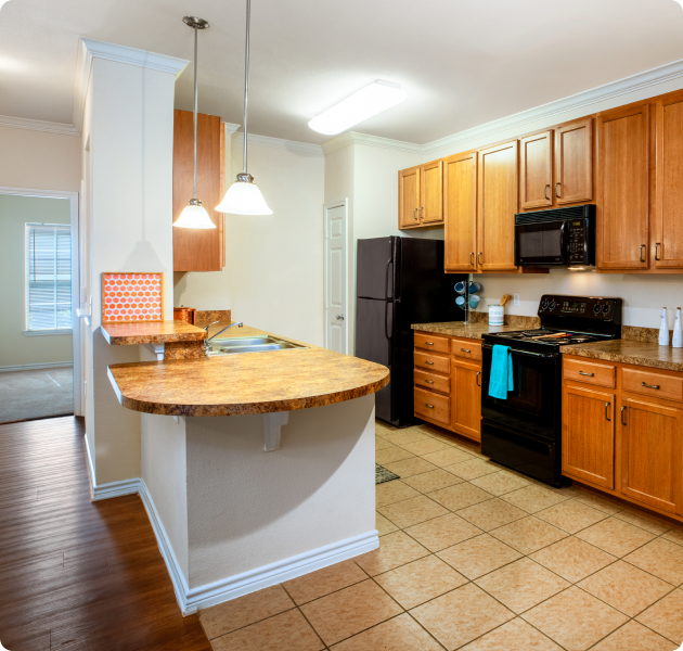 Apartment kitchen with hanging light fixtures over breakfast bar countertop, wooden cabinets and upgraded appliances at MAA Canyon Creek luxury apartments in Austin, TX