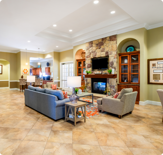 Modern community clubhouse with multiple seating areas next to a wall-mounted TV above a brick fireplace on tile floors at MAA Canyon Creek luxury apartments in Austin, TX