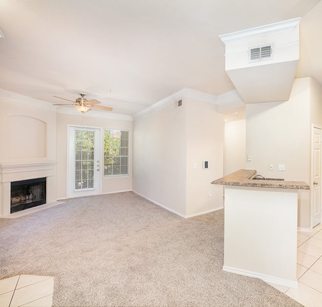 Apartment empty living room area with a ceiling fan and French glass door with a fireplace next to kitchen area at MAA Canyon Pointe luxury apartments in Austin, TX