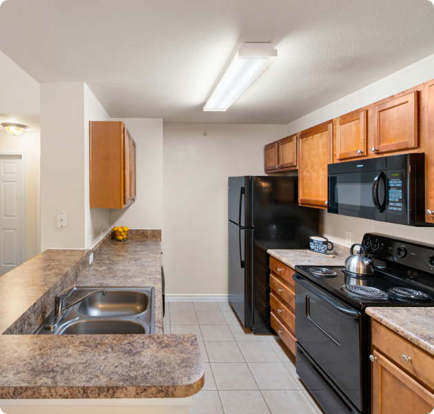 Apartment kitchen with wooden cabinets, upgraded appliances and stainless steel sink on tile flooring at MAA Cedar Park luxury apartments in Cedar Park, TX
