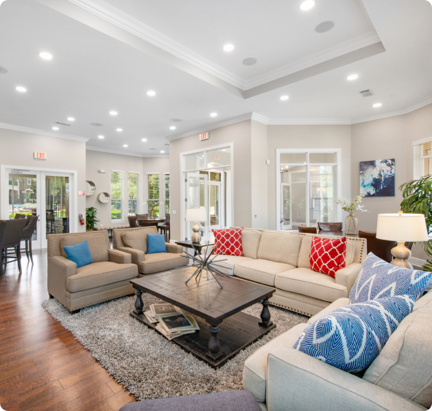 Community clubhouse with multiple seating areas, couches around a wood coffee table on an area rug on wood floors at MAA Cedar Park luxury apartments in Cedar Park, TX