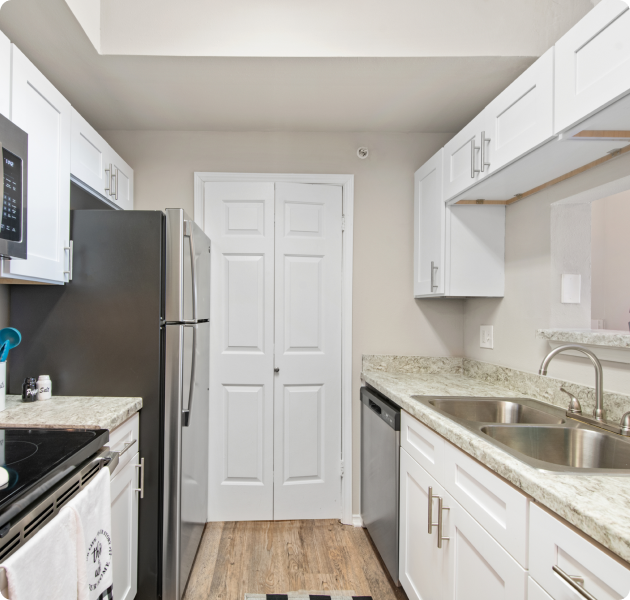 Apartment kitchen with white cabinets, granite countertops and stainless steel appliances on wood floors at MAA Quarry Oaks luxury apartments in Austin, TX.