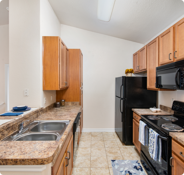 Apartment kitchen with tan wood cabinets, upgraded appliances, and a double stainless steel sink on tile floors at MAA Round Rock luxury apartments in Round Rock, TX.