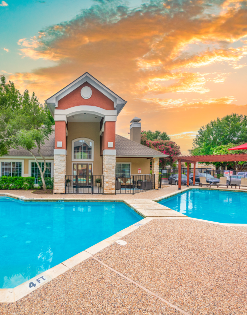 Gated swimming pool next to community clubhouse with a sunset sky at MAA Sierra Vista luxury apartments in Round Rock, TX