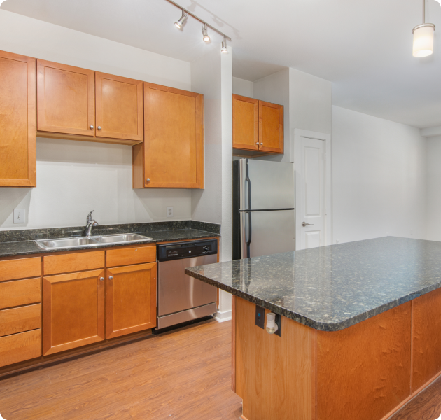 Apartment kitchen with hanging light fixtures, wooden cabinets, stainless steel appliances with a kitchen island on wood floors at MAA West Austin luxury apartments in Austin, TX