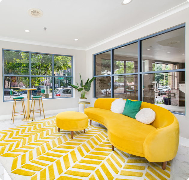 A yellow couch situated in front of a large window in the community center at MAA Abbey luxury apartments in Dallas, TX